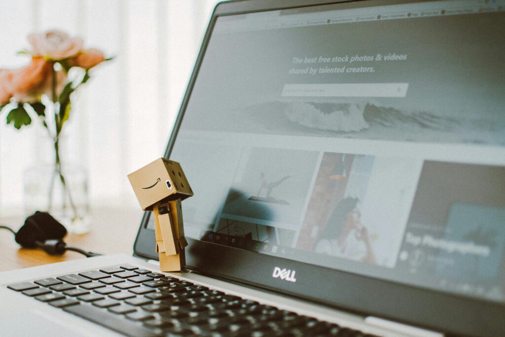 pexels-photo-2363482-2363482 A small toy figure stands on a laptop keyboard with flowers in the background.